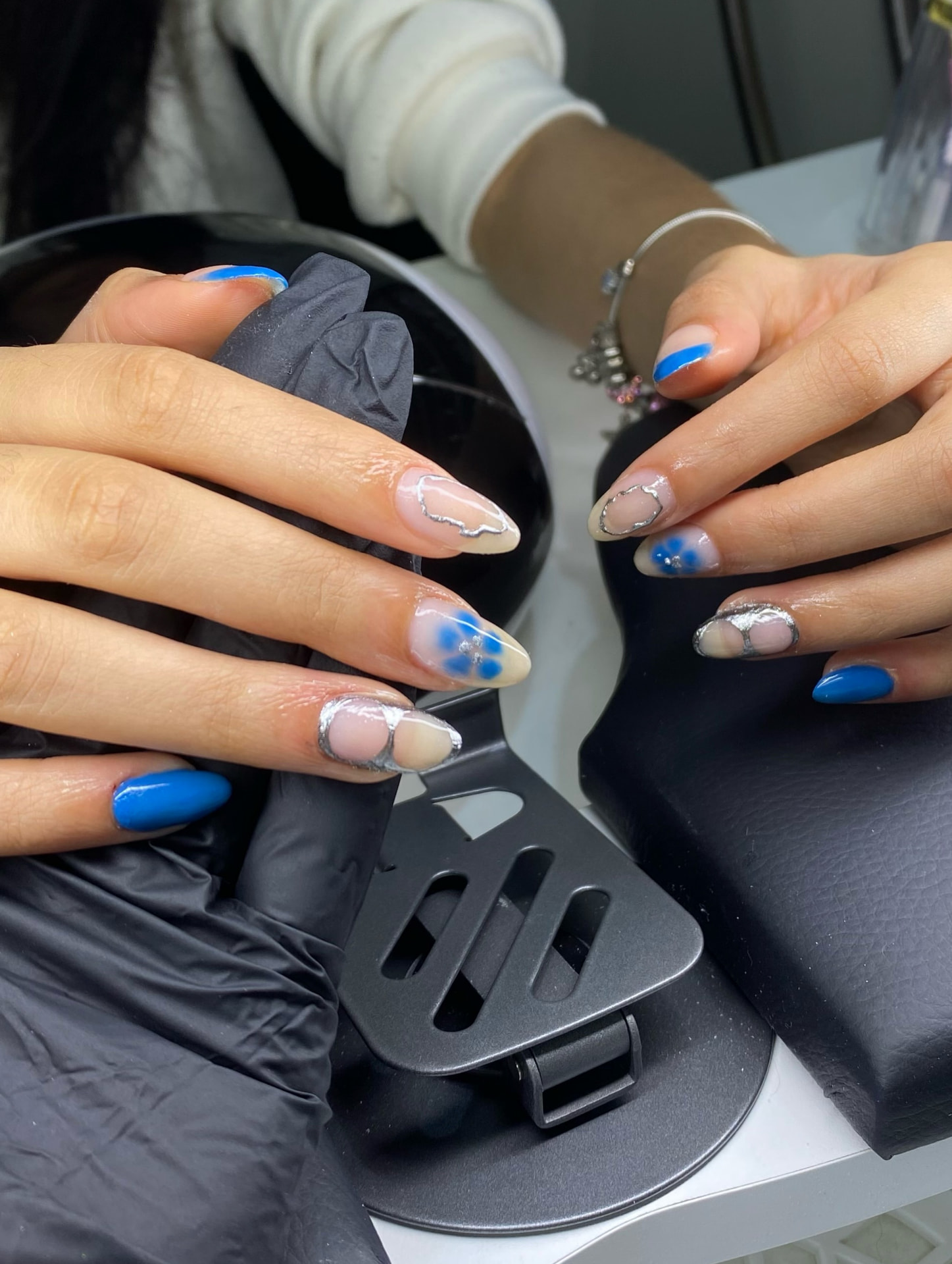 Duas mãos com nail arts em azul, prata e nude